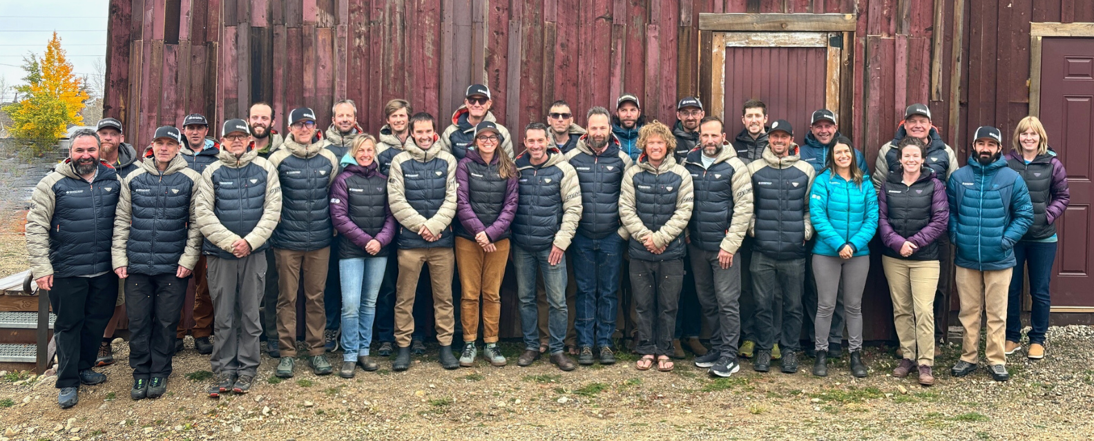 CAIC team posing in front of red barn wearing CAIC coats. 