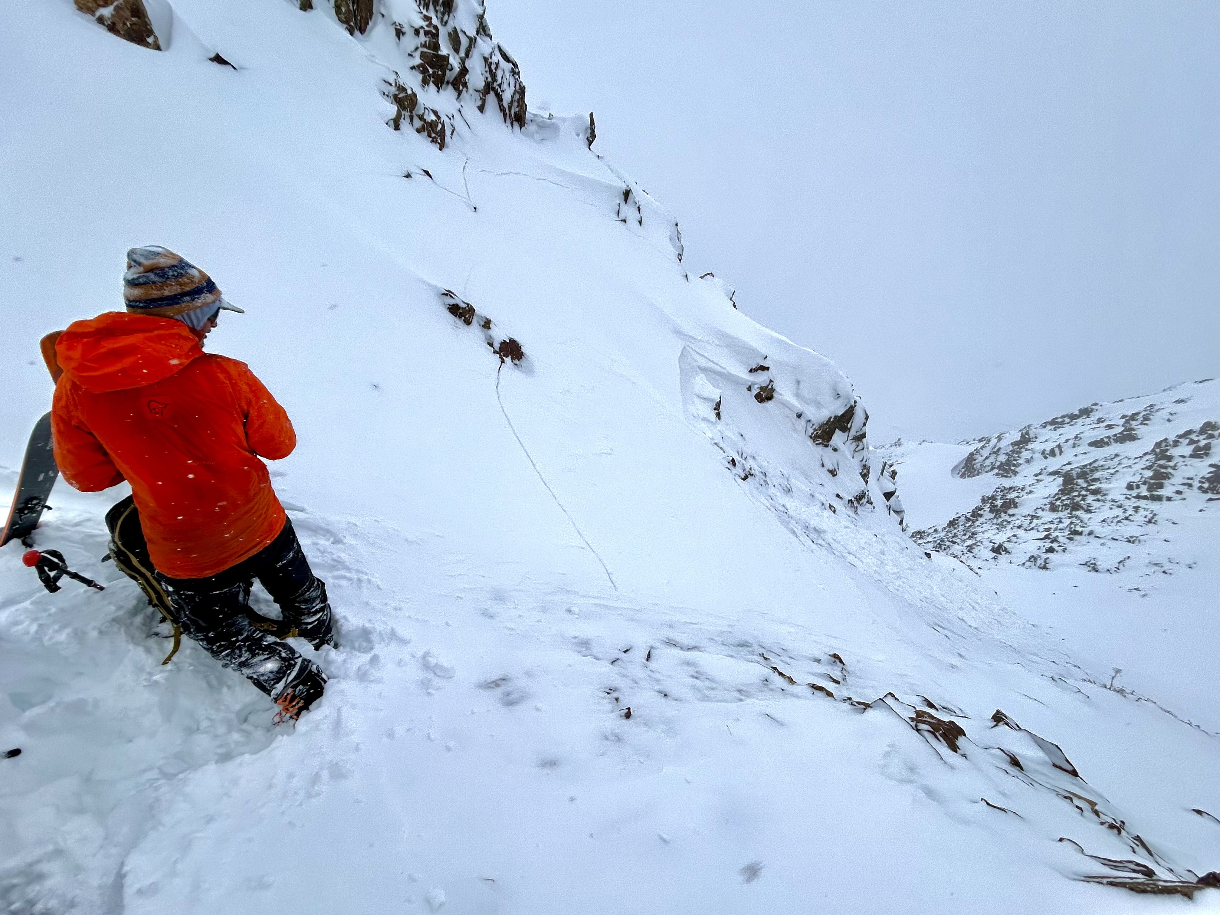 Skier in red coat looking downhill at small wind slab avalanche