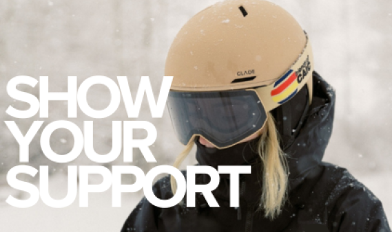 Close up picture of woman with tan ski helmet, black goggles and a coat with "show your support" in white letters