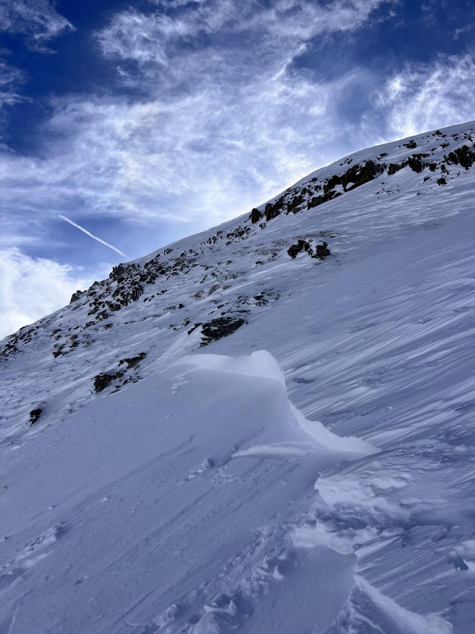 close-up of a wind slab avalanche crown below some rocks under a moody sky. 