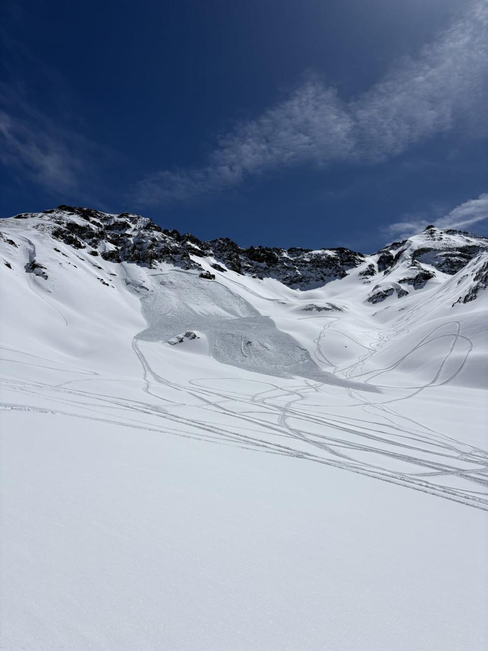 Avalanche on a nearby slope surrounded by tracks on a bright sunny day.