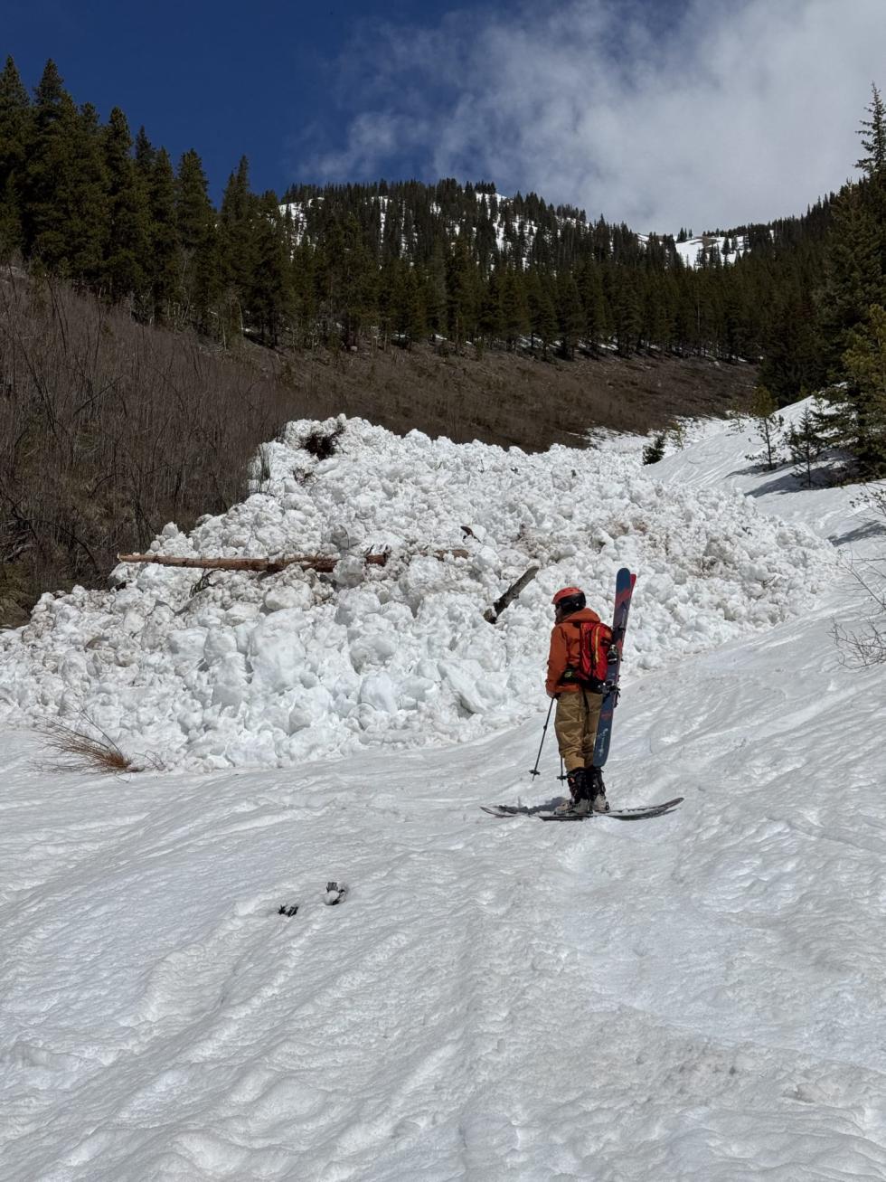 Person standing near a pile of avalanche debris on a sunny day.